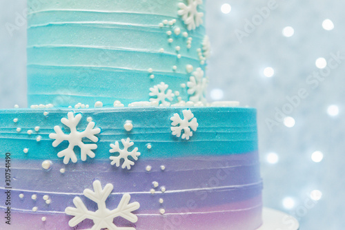 Cropped photo cake show details of wonderful blue and purple birthday party cake decorated with snowflakes. Two storey cake on blue background with defocused lights. Studio photo with selective focus photo