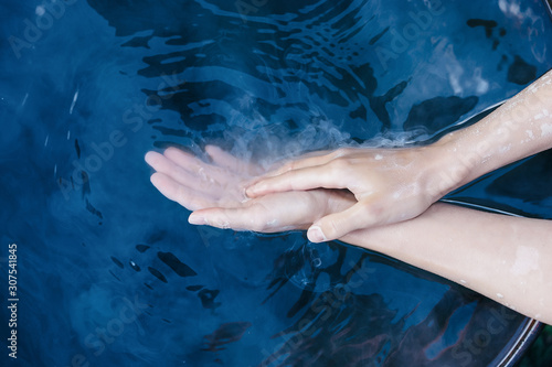 A pair of elegant female hands in dried clay in the blue water. Ceramics production. Creativity and hobby. The concept of clearing and getting rid of the past. Classic background