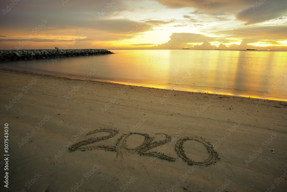 Fototapeta premium Welcoming new year concept. Welcome 2020 written on sandy beach with beautiful sunset background.