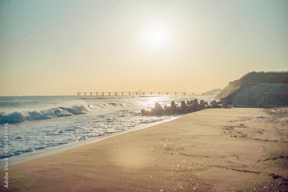 The sun rises on sandy beaches, distant boardwalks, and breakwaters.