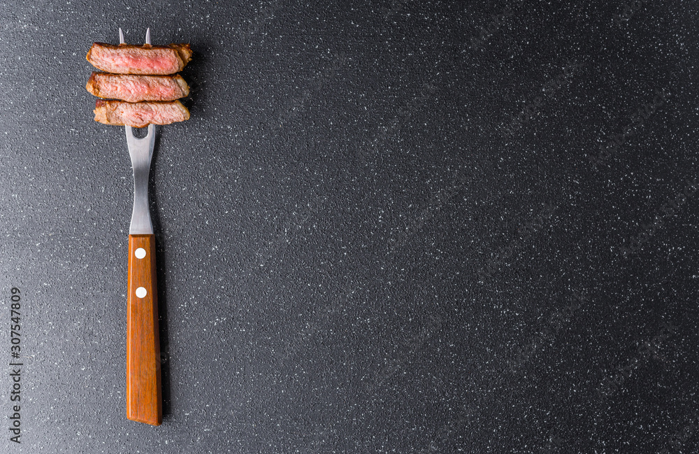 New york strip loin beef steak on a meat fork against black stone background New york strip loin beef steak on a meat fork against black stone background