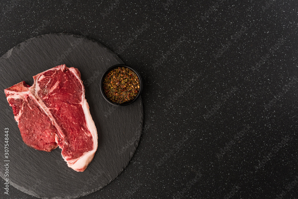 Raw t-bone porterhouse beef steak meat with chimichurri sauce against black stone background