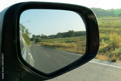 Car's side view mirror. On a rural road area with pastures.