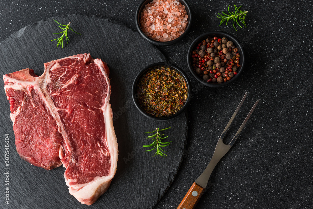 Raw t-bone porterhouse beef steak meat with chimichurri sauce against black stone background Raw t-bone porterhouse beef steak meat with chimichurri sauce against black stone background