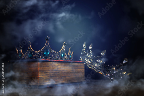 low key image of beautiful queen/king crown over old book and wooden table. vintage filtered. fantasy medieval period. mist and fog