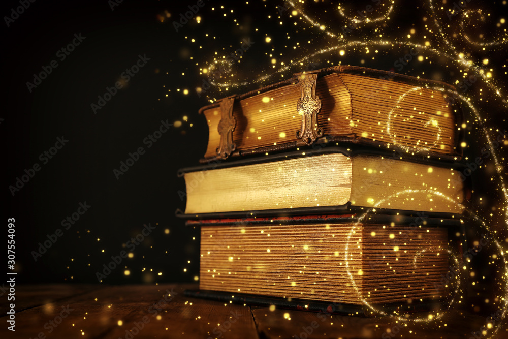 stack of antique books on old wooden table. fantasy medieval period and religious concept. Glitter sparkle lights - obrazy, fototapety, plakaty 