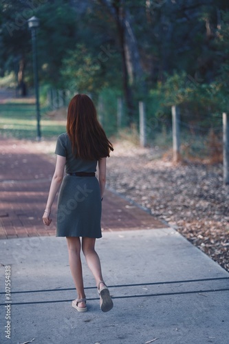  Brown haired tall and very slim woman is walking in the green park. Khaki dress and leather belt. Safari outfit