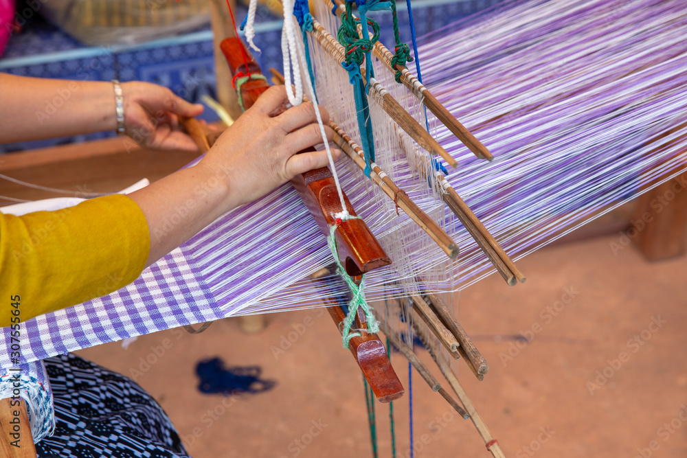 Cotton weaving. Woman hand weaving cotton on manual loom. Thai cotton  handmade. Homespun fabric process. The process of fabric weaving in vintage  weaver machine. Selective focus. Stock Photo