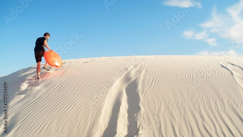 Happy man on sand in white sands dunes national monument park in New Mexico on disk sled sliding down hill panning pov