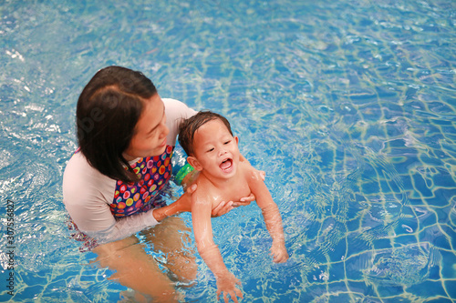 Asian Mother and baby boy relaxing in swimming pool training.