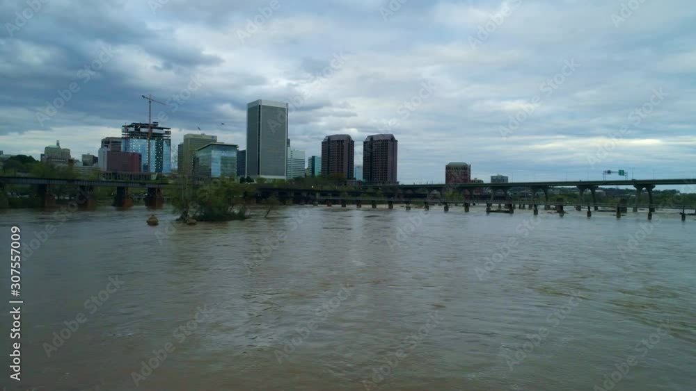 Low aerial flight laterally over the James River with the waters high and brown, and a gull flies overhead Low aerial flight laterally over the James River with the waters high and brown, and a gull flies overhead
