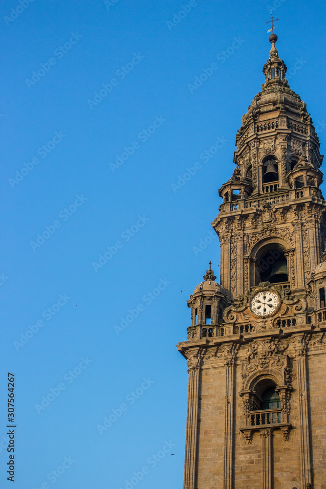 Santiago de Compostela, Spain -10/19/2018: Clock tower with bell and cross on clear blue sky background. Exterior of famous cathedral on sunny day. Ancient religious architecture. Unesco heritage.