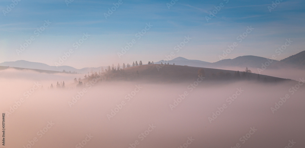Top of the hill wrapped with the morning fog at Carpathian mountains. Beautiful sunrise over mountain.