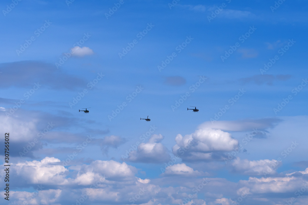 The link of three helicopters fly under white clouds in the blue sky.