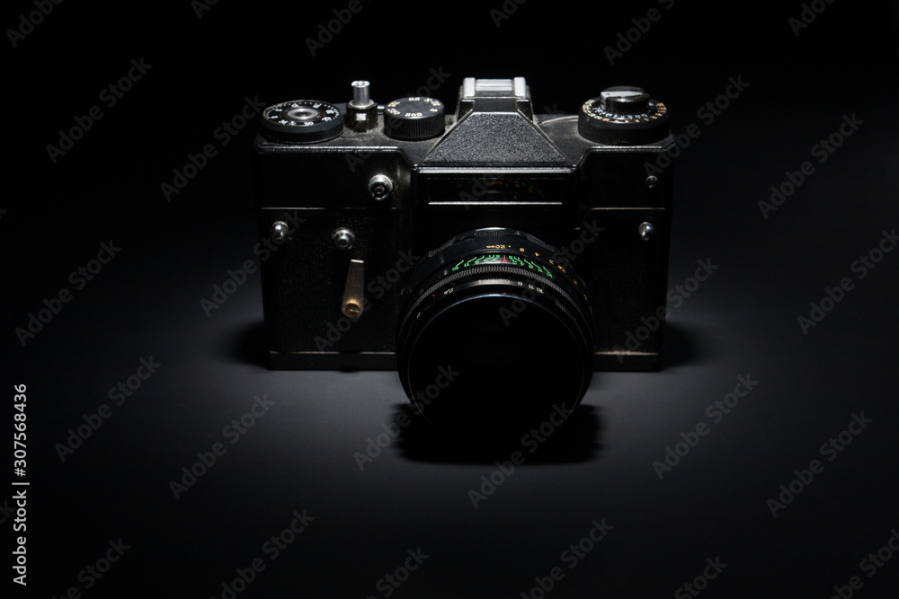 Old black film camera on black background under spot light.