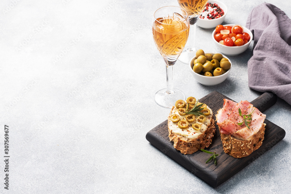 Wholegrain bread sandwiches with cream cheese, bacon and olives on a wooden cutting Board. A glass of white wine. Gray concrete background with Copy space. Wholegrain bread sandwiches with cream cheese, bacon and olives on a wooden cutting Board. A glass of white wine. Gray concrete background with Copy space.