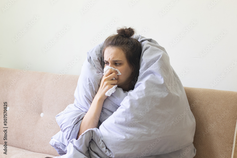 Sick young woman in blanket sits at home with a runny nose. Sick young woman in blanket sits at home with a runny nose.