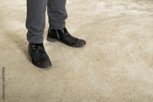 Men's feet in black boots and dark denim pants on a concrete background. Copy space for advertising. Negative space.