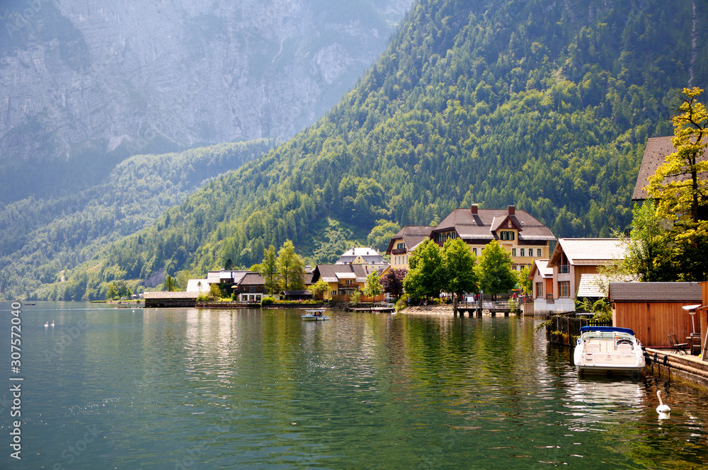 Houses and pier on the shore of the lake. Mountains with forest in the background. Boats and catamarans on the lake.
