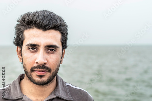 closeup of face of an Arab man having beard and wearing western clothes and feeling happy in Saudi Arabia and see in the background 