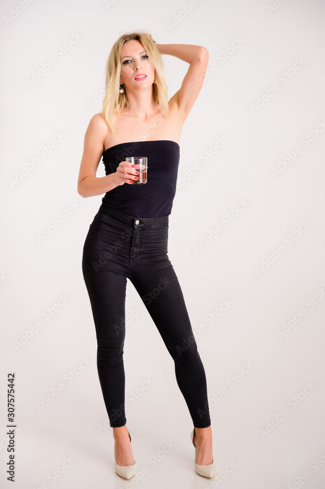 The concept of alcoholic relaxation. Full-length portrait of a pretty woman model with excellent make-up, beautiful hair on a white background standing with a glass of whiskey in her hands. The concept of alcoholic relaxation. Full-length portrait of a pretty woman model with excellent make-up, beautiful hair on a white background standing with a glass of whiskey in her hands.