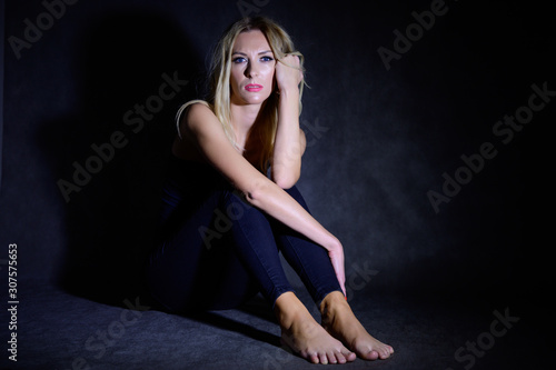 Artistic portrait of a pretty woman model sitting on the floor in the dark with excellent makeup, beautiful hair. Sitting in front of the camera.