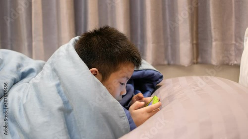 asian chinese boy playing smartphone on bed, kid use phone and play game, addicted game and cartoon, 