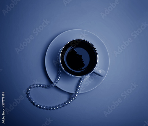 A cup of espresso with reflection of a female face silhouette, pearl beads and a few beads in blue tones. Flatlay.