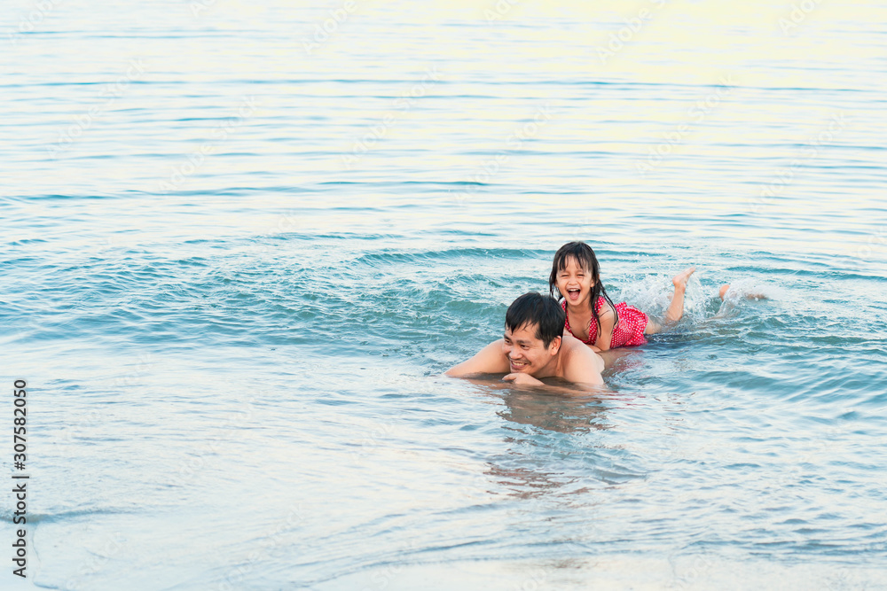 Asian father and daughter are playing together in the sea water with the background of beautiful sunlight, concept of love and relation in family lifestyle.