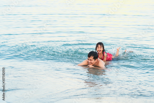 Asian father and daughter are playing together in the sea water with the background of beautiful sunlight, concept of love and relation in family lifestyle. © Sukjai Photo