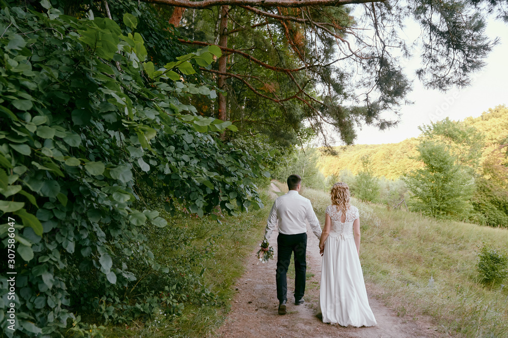 Full length body portrait of young bride and groom walking in forest, back view. Happy wedding couple, copy space Full length body portrait of young bride and groom walking in forest, back view. Happy wedding couple, copy space