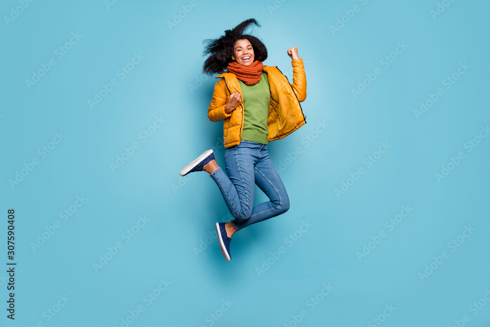 Full size photo of pretty dark skin lady jumping high celebrating sale shopping black friday beginning wear overcoat jeans sweater scarf isolated blue color background Full size photo of pretty dark skin lady jumping high celebrating sale shopping black friday beginning wear overcoat jeans sweater scarf isolated blue color background