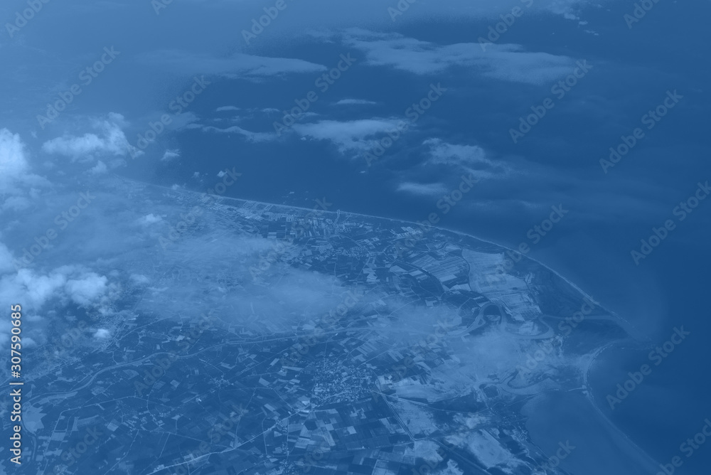 Top view from landing airplane in trendy monochrome blue and calm color background. Window plane with copy space. Aerial view of cloud, sea, ocean and city landscape