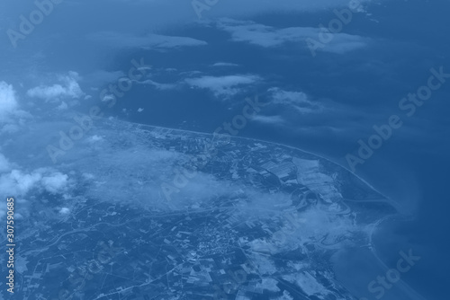 Top view from landing airplane in trendy monochrome blue and calm color background. Window plane with copy space. Aerial view of cloud, sea, ocean and city landscape © jchizhe