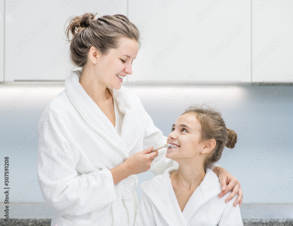 Happy family at home. Smiling mom teaching her young daughter how to brush teeth with toothbrush Happy family at home. Smiling mom teaching her young daughter how to brush teeth with toothbrush