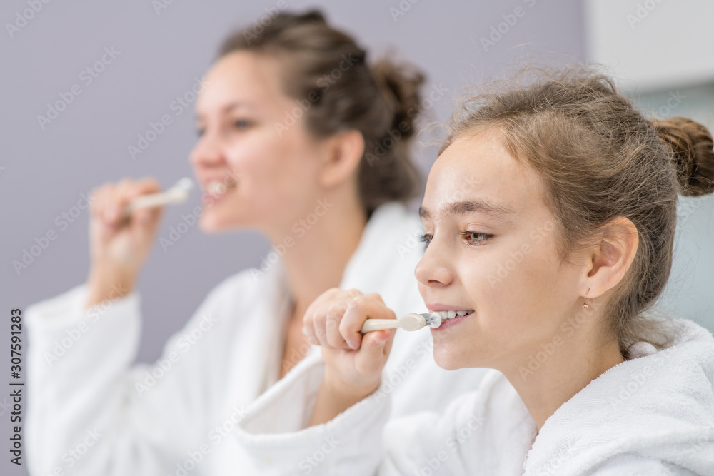 Mom and her daughter brush their teeth in front of the bathroom mirror Mom and her daughter brush their teeth in front of the bathroom mirror