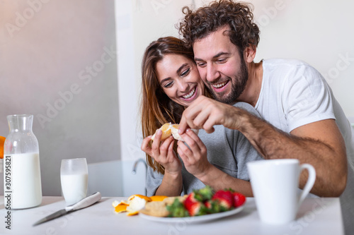 Beautiful young couple is looking at each other and feeding each other with smiles while cooking in kitchen at home. Loving young couple embracing and cooking together  having fun in the kitchen