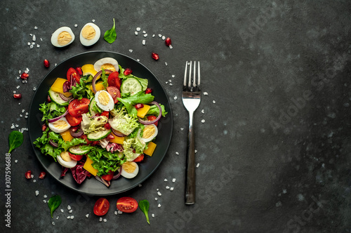 Salad with pomegranate, eggs, tomatoes, fresh cucumbers, onions, sesame and bell pepper, spices on a stone background. Healthy food. With copy space for your text.