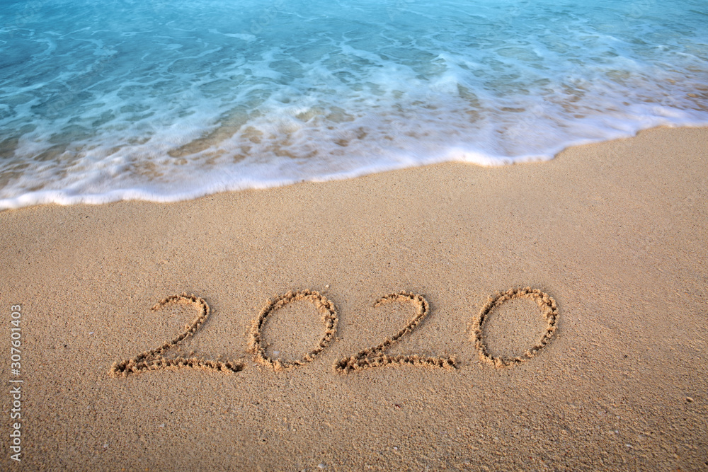 New Year 2020 is coming concept. 2020 inscription written in the wet beach sand with sea water wave New Year 2020 is coming concept. 2020 inscription written in the wet beach sand with sea water wave