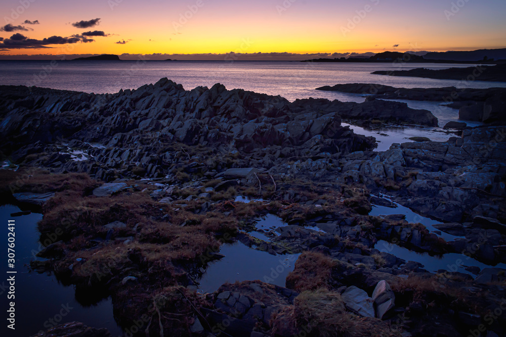 Tranquil sunset scene on rocky beach, on west coast of Scotland.Colourful sky at twilight and puddles of water among rocks during low tide.Beauty in nature.