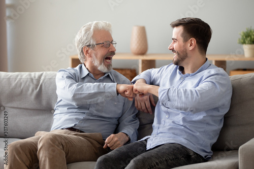 60s man and millennial guy giving fist bump sitting indoors