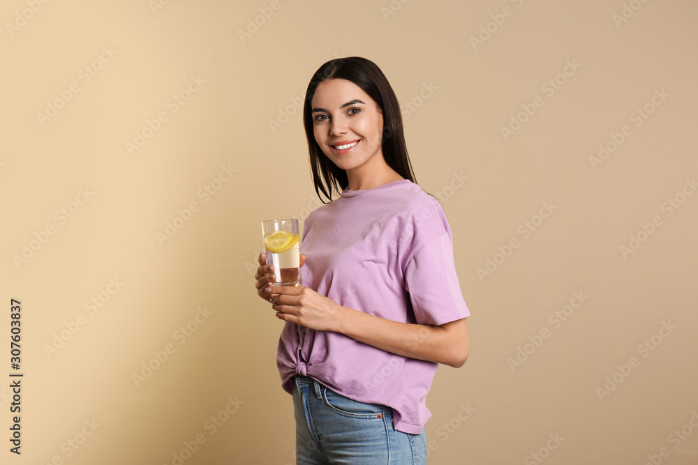 Beautiful young woman with tasty lemon water on beige background Beautiful young woman with tasty lemon water on beige background