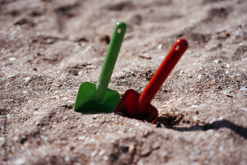 two plastic shovels red and green in the sand on the beach two plastic shovels red and green in the sand on the beach