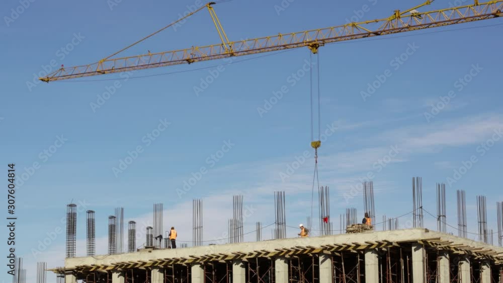 Construction site with workers over terrace loading tower crane ballet with bricks on blue sky background, wide static shot