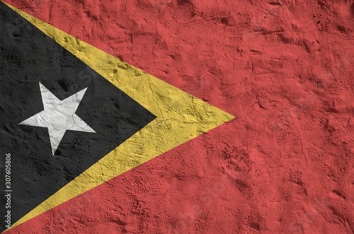 Timor Leste flag depicted in bright paint colors on old relief plastering wall. Textured banner on rough background photo