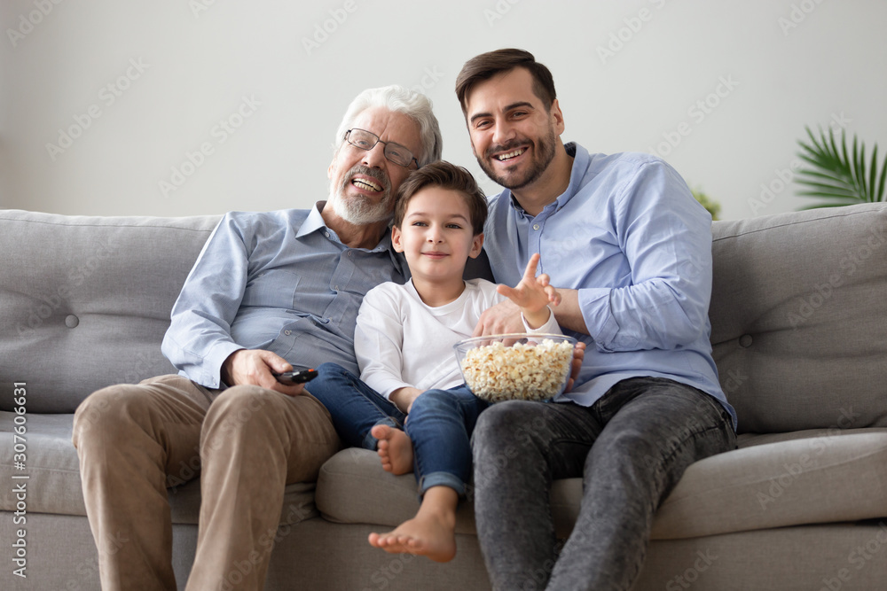 Cheerful grandfather grownup son and grandchild watching TV eating popcorn Cheerful grandfather grownup son and grandchild watching TV eating popcorn