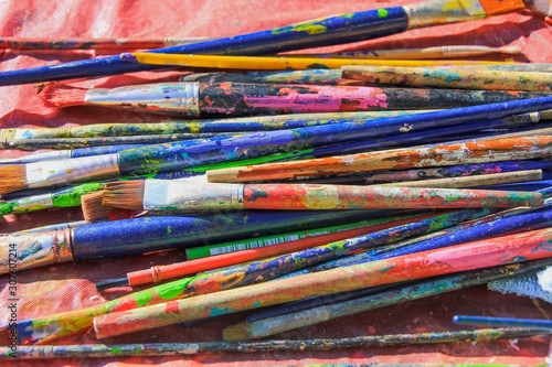 Bright multicolor paint brushes of the artist lie on the old table in the workshop.Creative mess.