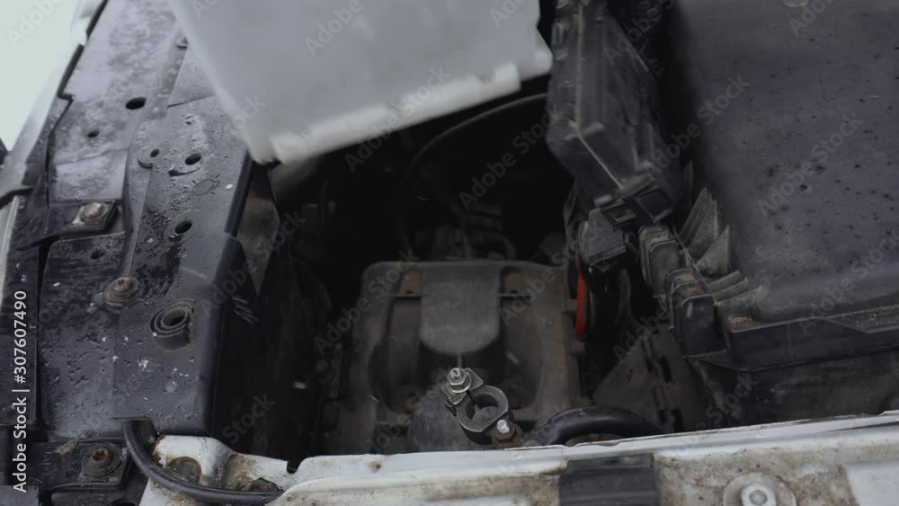Man removes Discharged automotive battery from car to fix or repair in winter. Malfunction or problem with automobile. Hood or bonnet raised up in daytime in parking. Closeup of lead-acid battery Man removes Discharged automotive battery from car to fix or repair in winter. Malfunction or problem with automobile. Hood or bonnet raised up in daytime in parking. Closeup of lead-acid battery