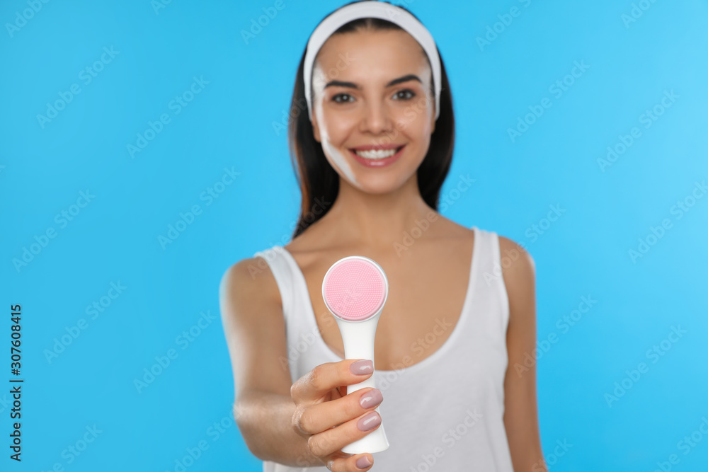 Young woman holding facial cleansing brush on light blue background. Washing accessory Young woman holding facial cleansing brush on light blue background. Washing accessory