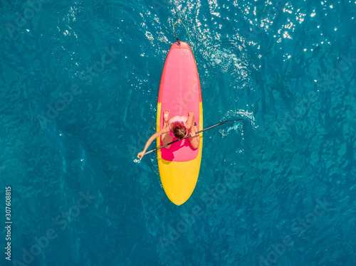 Canvas Print Attractive woman in swimwear floating on stand up paddle board on a quiet blue ocean